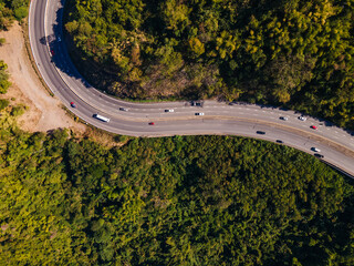 the aerial view of the countryside curve road near the green forest on the hill