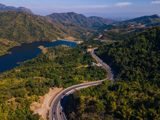 the aerial view of the countryside curve road near the green forest on the hill