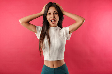 Happy young woman wearing white ribbed crop isolated over red background emotional surprised woman holding hands by the head and looking at camera. Very happy and cannot believe it.
