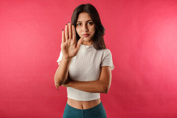 Wearing white ribbed crop isolated over red background showing with palm hand stop sign gesture. No...