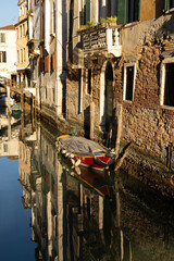 Boats covered from rain parked in the water next to the house in canal of Venice. Water transport and transportation theme. Morning in Venice.