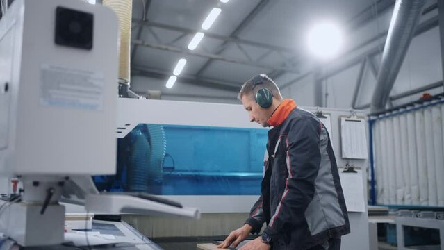 high-skilled worker is adjusting CNC milling machine in workshop of furniture plant, cut chipboard