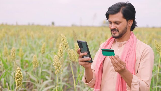 Young farmer at field with making online payment using credit card on mobile phone - concept of e-commerce, online banking service and technology