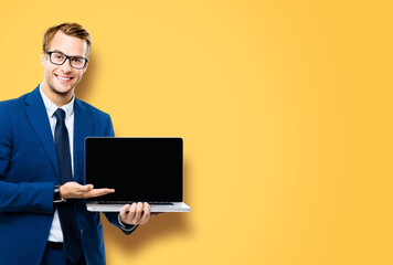 Smiling business man in glasses spectacles, suit show laptop with empty mockup screen, isolated over yellow background, with copy space. It expert,  technician repair service, tech support maintenance