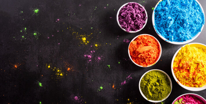Top view of colorful holi powder with multicolored holi paint on dark background. Happy holi festival decoration concept. © Siam