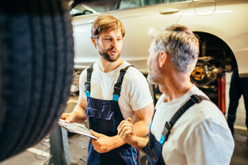 Car service station. Two different age bearded attractive mechanics men standing and looking at...