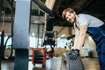 Car service, repair, maintenance and people concept. Tire repairer checking the tire integrity. Portrait of a smiling mechanic at work in his garage