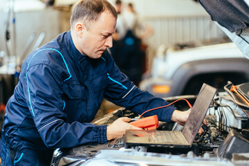 Skillful confident auto electrician using a computer laptop to diagnosing and checking up on car...