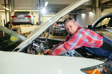 Portrait of mature middle age man mechanic in plaid shirt working at garage. Mechanic worker at car repair service and auto store shop.