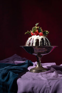 Traditional festive Christmas fruit pudding dessert, decorated with cherries and leaves, set in a classic warm red and purple background