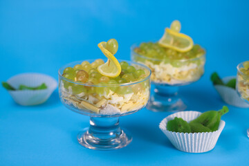 meat chicken salad in layers in a transparent glass with green grapes and lemon slices next to kiwi on a blue background. for labels, screensavers, business cards, banners, menu signs