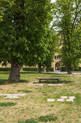 A bench in the courtyard of a former school with high trees and old building