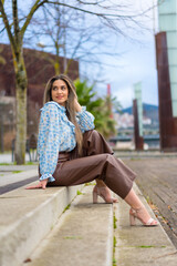 Young woman sitting in a park in the city, lifestyle concept, blue shirt and brown pants