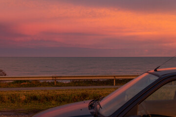 Sunset over the road, the sea and a car