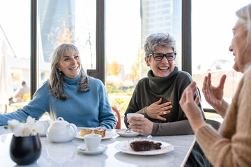 Group of elderly women have breakfast in a cafeteria, three retired female friends are celebrating an anniversary drinking tea and coffee and eating chocolate cakes
