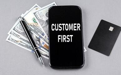 Credit card and text CUSTOMER FIRST on smartphone with dollars and pen. Business concept