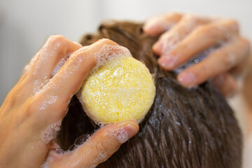 A man applies a solid shampoo bar to the hair. Man in the bathroom. Sustainable hair care,...