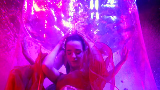 young woman diving in water of pool with magical pink illumination, neon violet lights