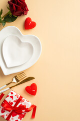 Valentine's Day concept. Top view vertical photo of heart shaped dishes knife fork giftbox candles and red rose on isolated pastel beige background with copyspace