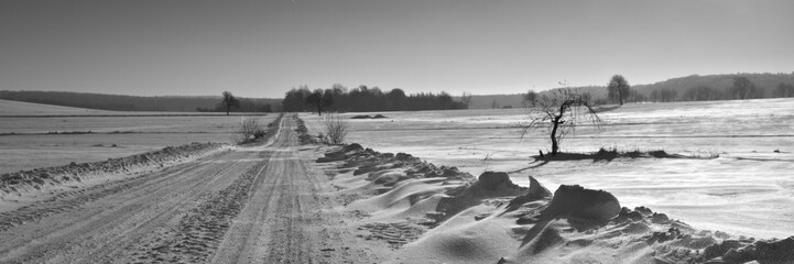 Winter road. Winter landscape of road. Snowy winter on the countryside, black and white picture. Highway leading through snowy fields. Drifts on the road.