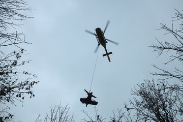 Emergency service paramedic with patient suspended by rope under helicopter. Rescue from difficult...
