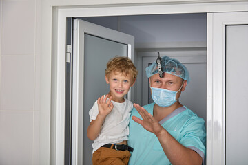 Funny boy in white T-shirt in arms of experienced pediatric surgeon enters the hospital room....