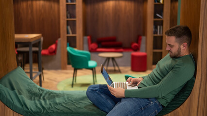 Caucasian bearded man working on laptop in modern coworking. 