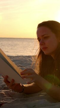 Young woman reads a book while lying on the beach at sunset - travel photography