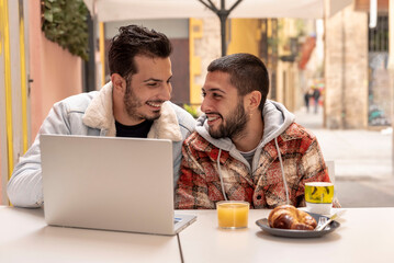 smiling gay couple at cafe using laptop