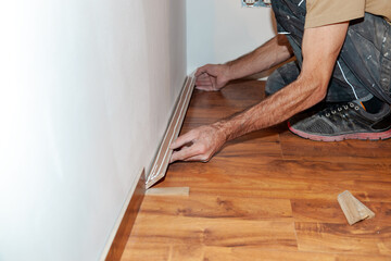 Worker, Carpenter installing laminate flooring. Installing molding trim Vinyl Plank Flooring.