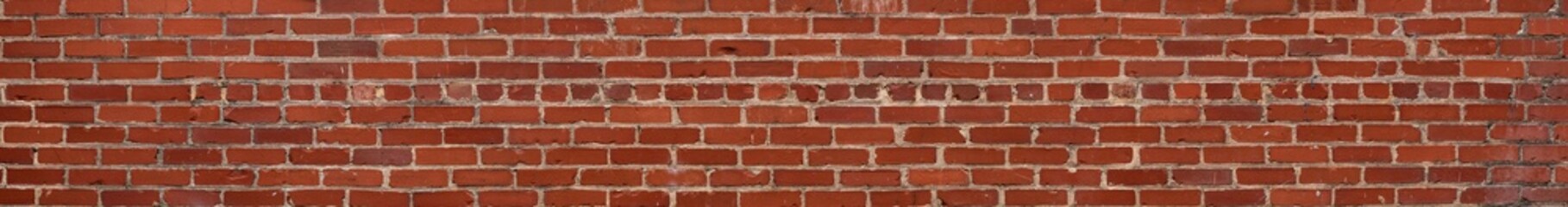 Extremely long thin panorama of red brick wall with irregular bricks in running bond pattern, horizontal aspect