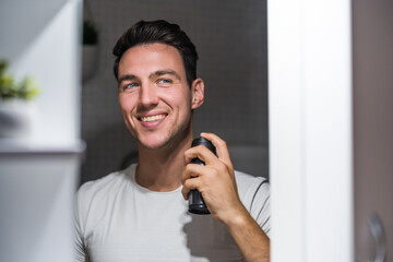 Man using deodorant  while looking himself in the mirror.