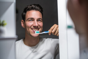 Man is  brushing teeth while looking himself in the mirror.