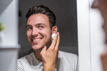 Man applying shaving cream while looking himself in the mirror.