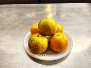 Naklejka na ściany i meble Five tangerines lined up on a small white plate. Plate with citrus fruits on a stainless steel table. Organic tangerines have uneven skin tone, a popular fruit with a sweet and sour taste. Scientific 