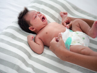 Cute baby girl crying while her mother changed her diaper. Mixed-race Asian-Australian infant dress up after bathing by her mommy. Health care concept..