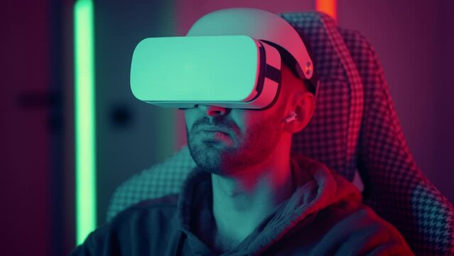 Cyber gamer in VR glasses plays virtual reality game in neon futuristic space. Gaming concept. Young handsome man looks around and shooting from virtual blaster gun.