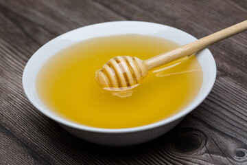 Honey with honey dipper in white bowl on wooden background.