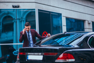 Entrepreneur(Businessman) standing in an urban area and wearing a suit and tie next to his limo...