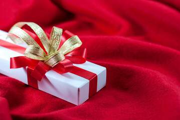 White gift box with red and gold ribbon on a red velvet floor with copy space, Valentine's day concept.