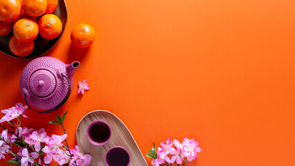 Chinese or lunar new year flat lay with mandarins, pink peach flower and tea set on orange...