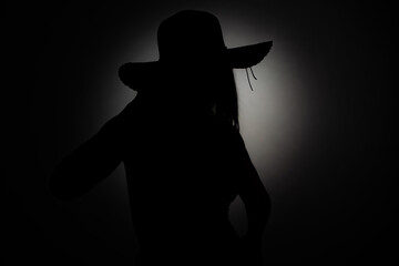 Dark silhouette of a girl with a hat in studio