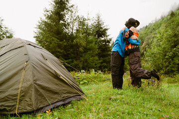 Young couple of travellers hugging while standing near camping tent
