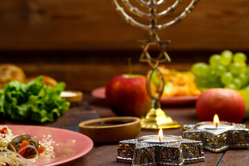 Burning candles in candlesticks Star of David on Shabbat Traditional Jewish food on the laid table, fruits, menorah.