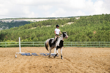 A young girl on a spotted horse is engaged in show jumping outdoors.