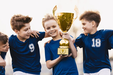 Happy young boys in sports team winning a soccer-football game and holding a golden trophy. Kids...