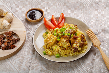 Rice in teriyaki sauce garnished with green onions on a wooden table next to soy sauce napkin and wooden fork next to anise saffron and ginger.