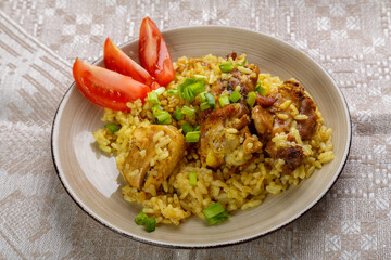 Rice chicken in teriyaki sauce garnished with green onions and tomatoes on a gray tablecloth.