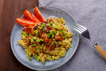 Rice chicken in teriyaki sauce garnished with green onions on a wooden table next to soy sauce on a napkin next to a fork.