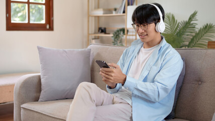 Young asian man with headphones relaxing at home. listening to music. man sitting on cozy sofa wearing headphone